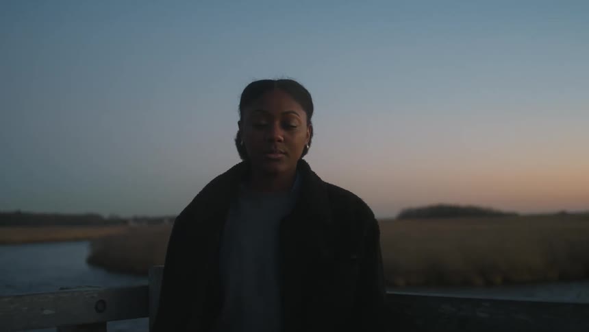 A black woman stands with her back to a stream at sunset