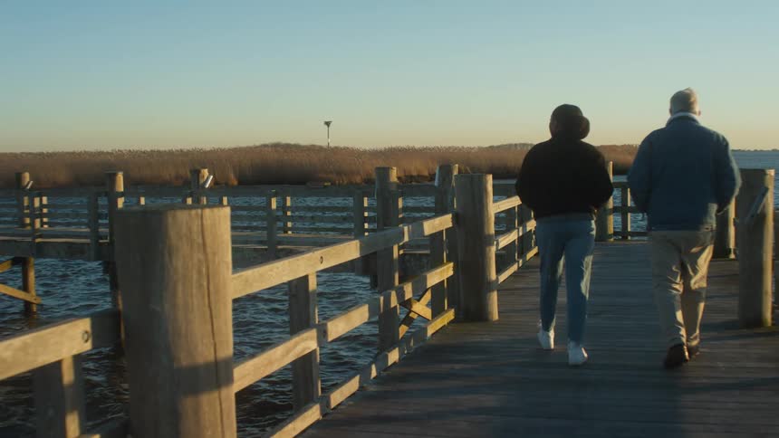 Man and woman walk along fenced pier over rippling water
