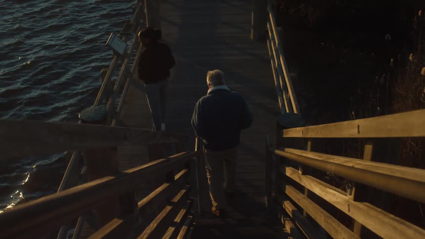 A man and woman descend stairs to a boardwalk on a lake at sunset