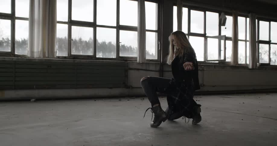 A woman dances in front of a wall of windows