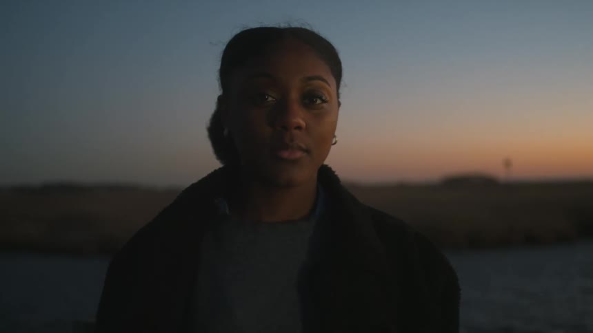 Woman poses near water under red tinted sky
