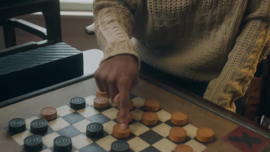 Woman sits at table moving a piece in a checker game