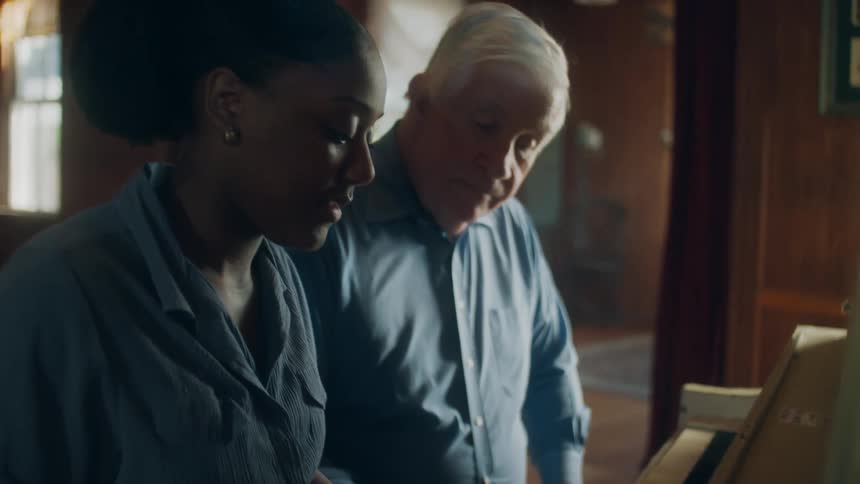 Elderly man watches a young woman play the piano