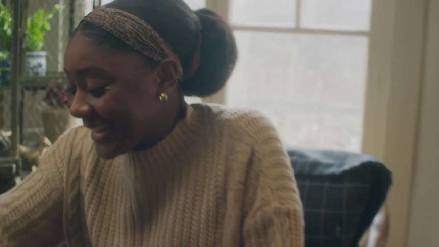 A young woman in a home laughs and talks as she takes her turn on a board game