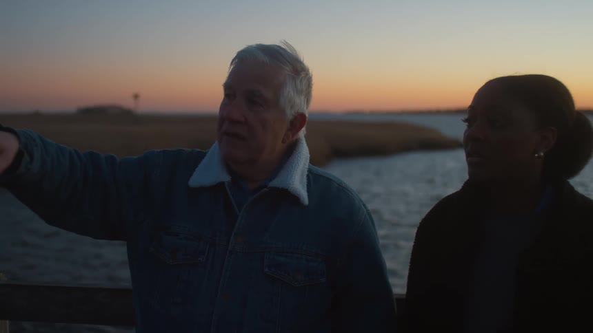 A man and woman chat as they stand along the shore at dusk