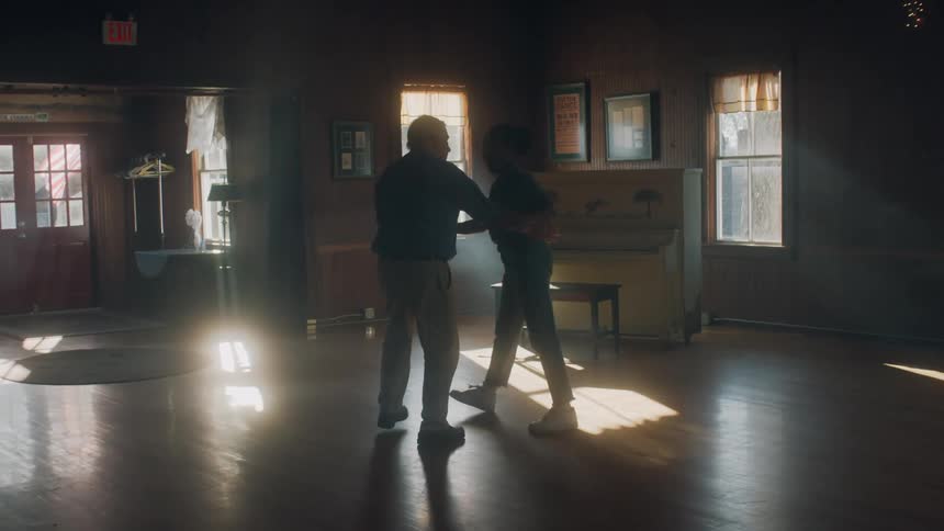 A man and woman dance in an open room with a piano
