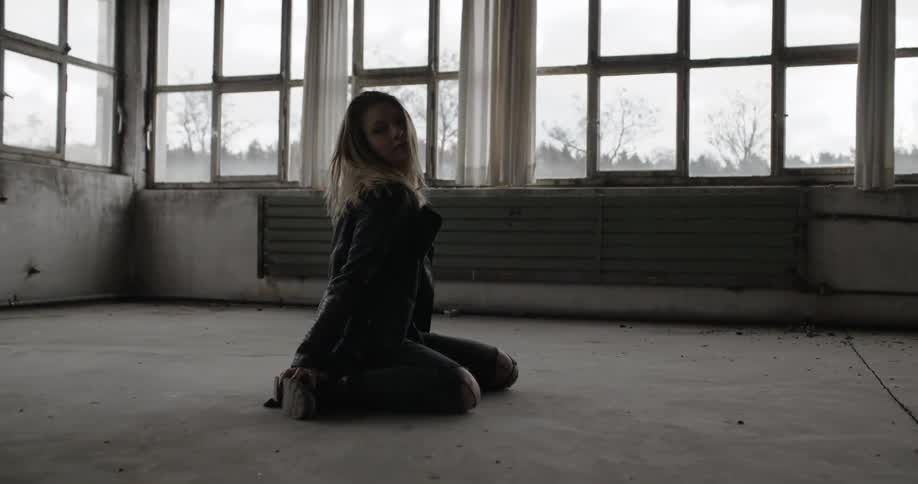 A woman in a black jacket kneels on the floor and stretches