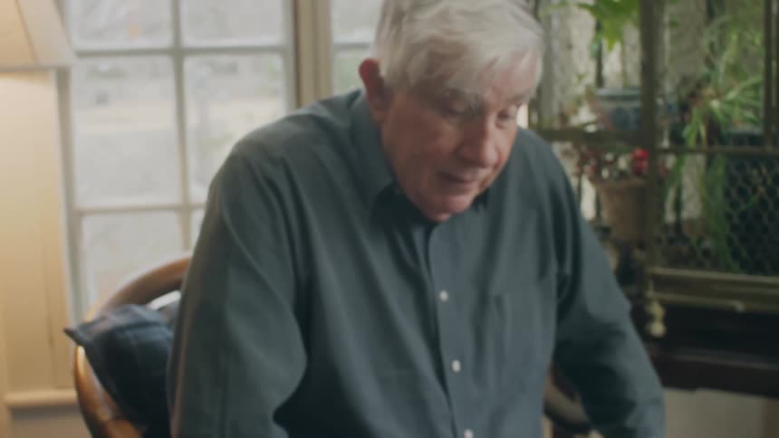 An elderly man and a young woman are sitting indoors playing checkers during the daytime