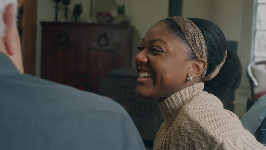 Black woman and old white man sitting in the couch at the living room having a conversation and laughing together