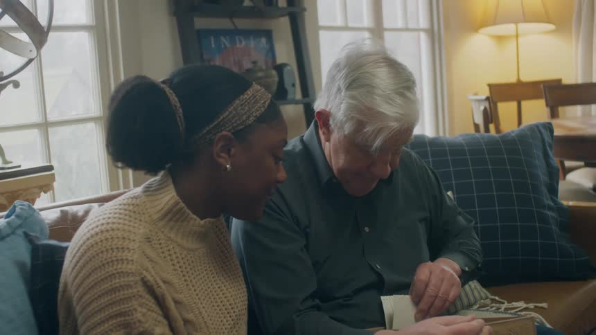 A man and woman look at photos inside a box as they sit on the couch