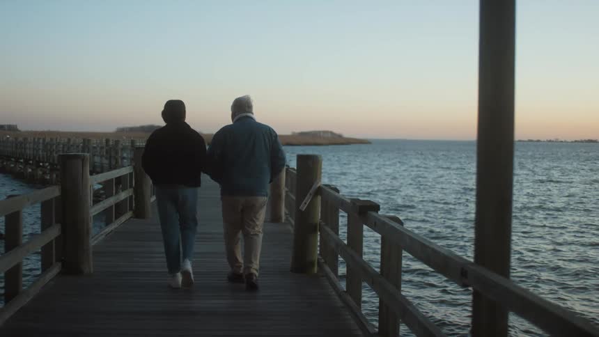 A man and woman talk as they walk on a wooden pier over the water at sunset