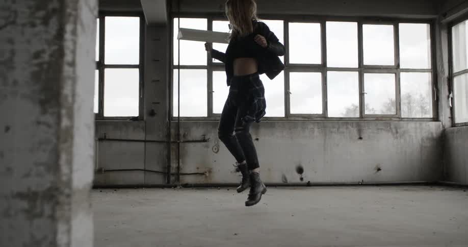 A woman jump up and dances in an abandoned warehouse