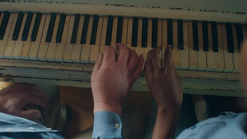 Elderly man with blue shirt and woman in blue shirt play piano together