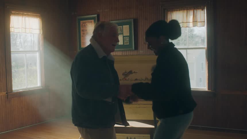 Man and woman dance in wood paneled room near piano