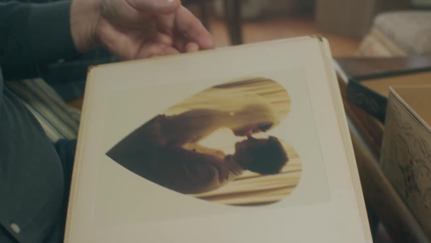 Man flips through photo albums as he talks to woman sitting on couch next to him