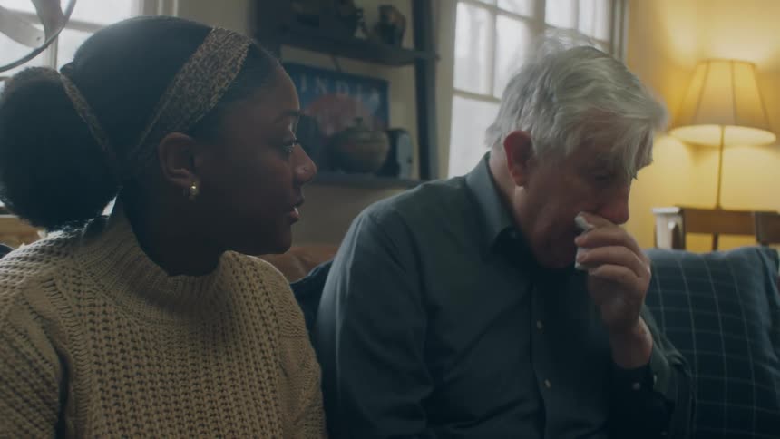 A man blows his nose while sitting on the couch with a woman