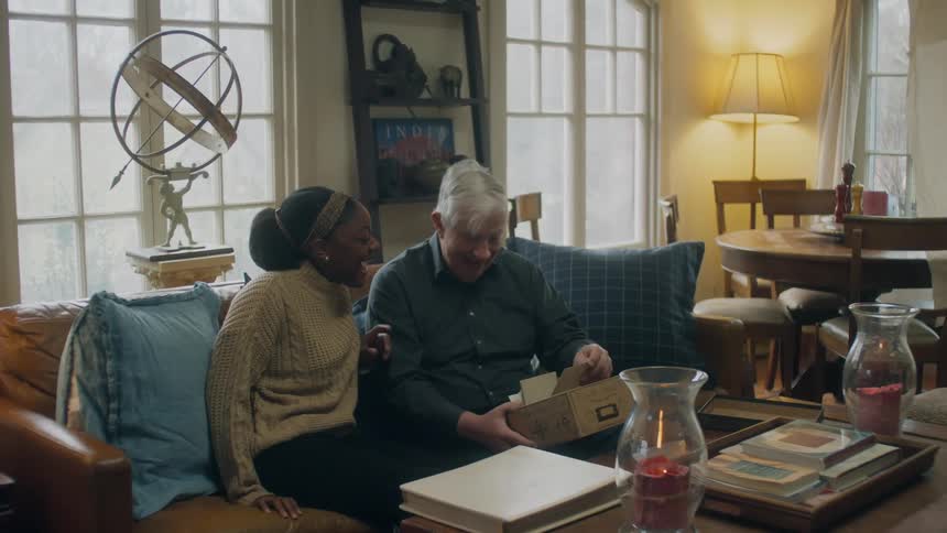 A man and woman look at photos on the couch
