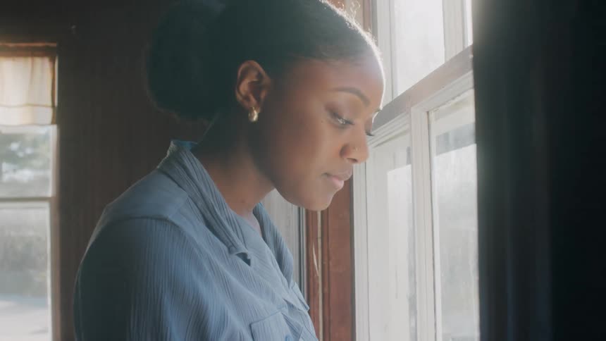 A pretty black woman looking out the living room window