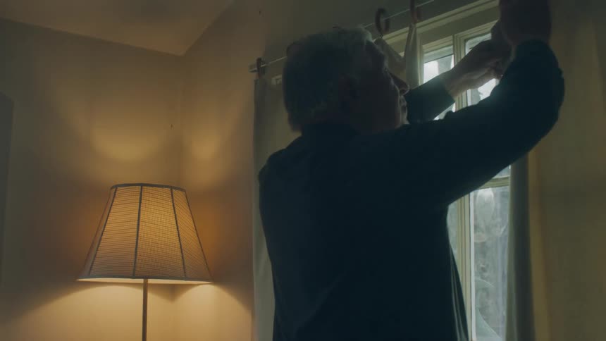 Elderly man with blue shirt closes the curtains