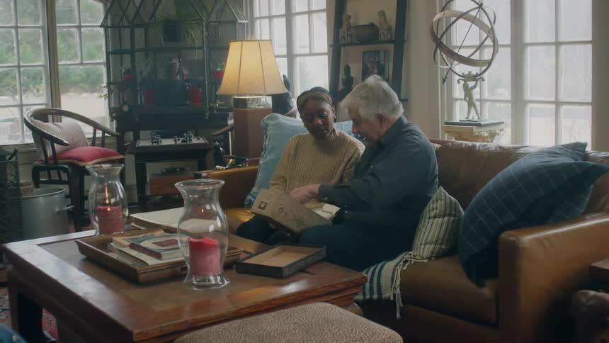 A man and woman go through photos in a box as they sit on the couch