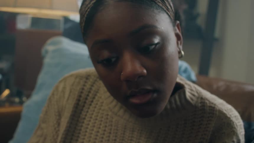 Black woman with an earring and a nose ring smiles while talking to the person next to her