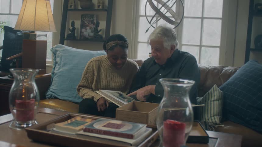 An elderly man sits with a young woman looking at a photo album