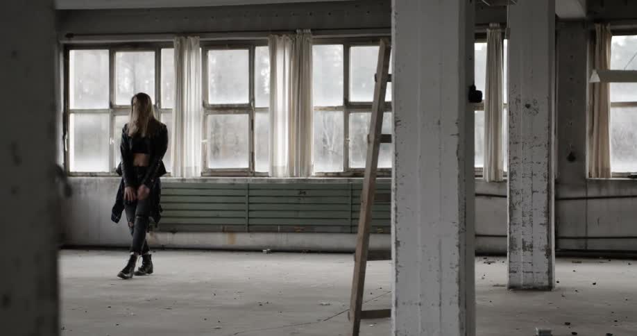 A blonde woman practicing dance moves in a vacant warehouse