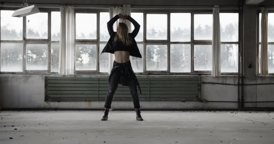 A young woman dances during the day in an empty building with lots of windows