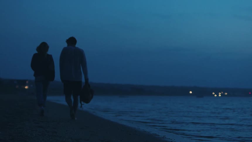 A couple walk along the beach at night