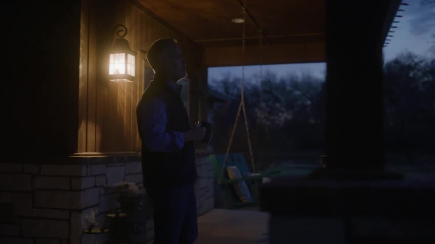A man walks onto his porch and looks out in front of him