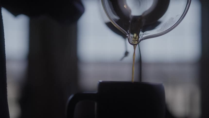 A man picks up a coffee pour over jug and pours it into a mug