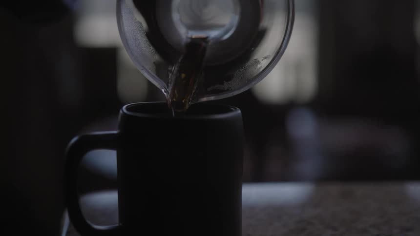 A man pours coffee from a carafe into a mug