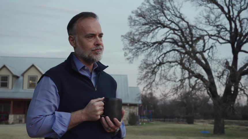 A man stands outside his home and drinks from a coffee cup