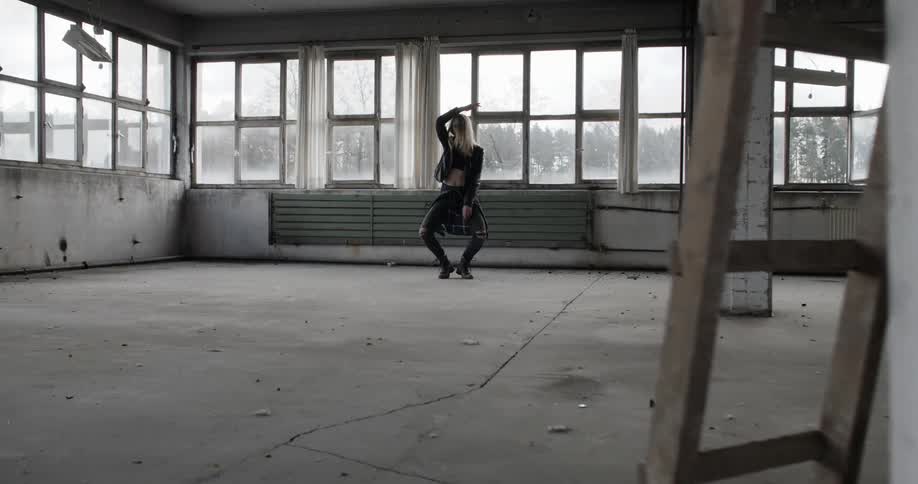 A woman in black dances in an empty warehouse