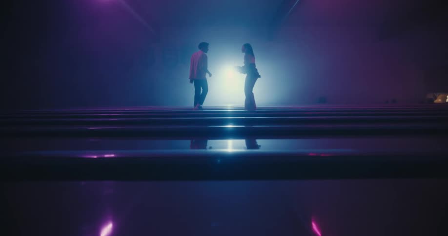 A young man and woman dance together on stage in front of a bright light
