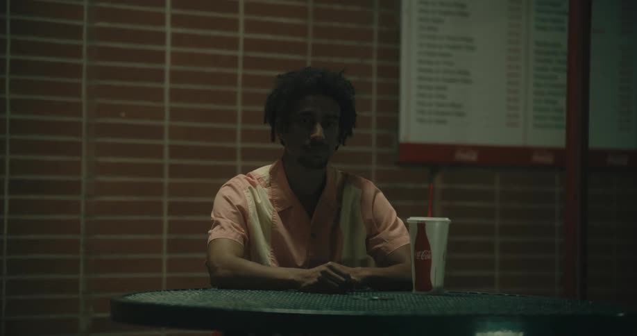 A man sitting at a table with bench seats and a large cola cup in front of him