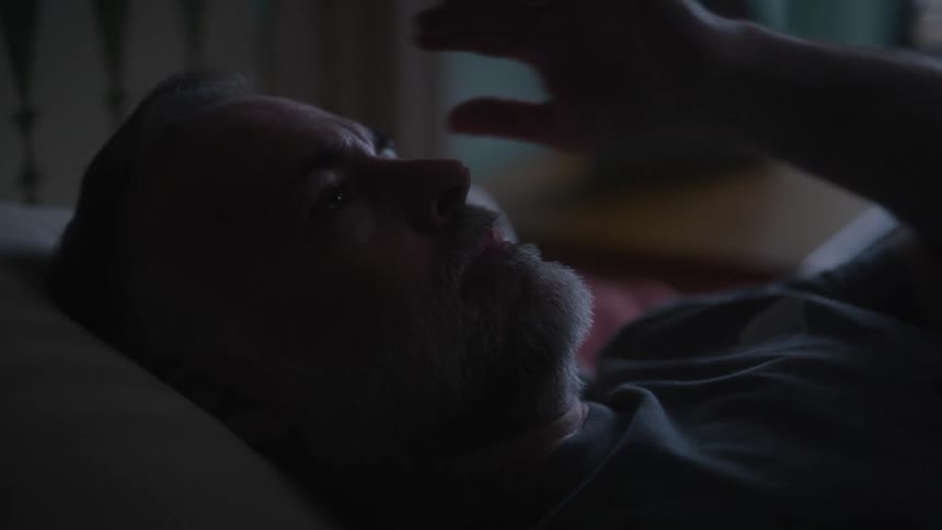 A man lying in bed rubs his face and beard with his hand