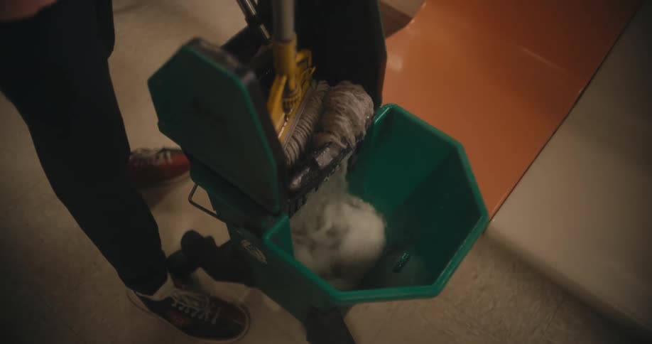 A person puts a mop in to a bucket of water and wrings it out