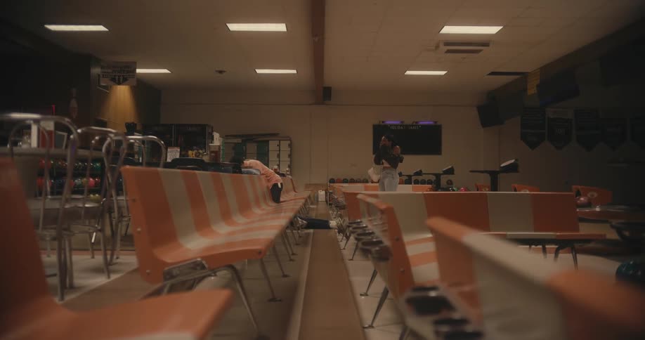 Woman stands back shocked as man arrives and attacks the man she was with from behind in empty bowling alley