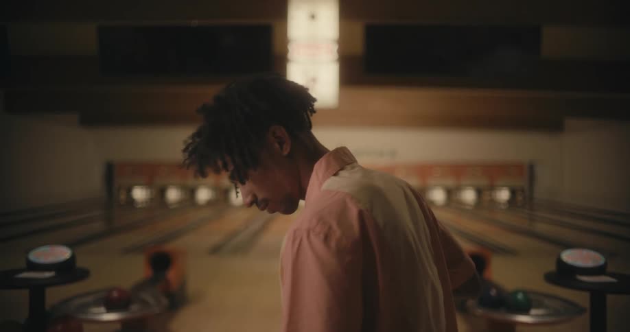 Black man sweeping the floor of an empty bowling alley when he suddenly stops because he heard something
