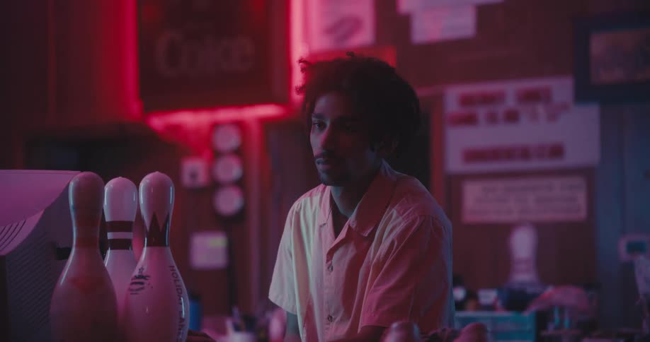 An employee standing behind a counter at a bowling alley looks off in to the distance