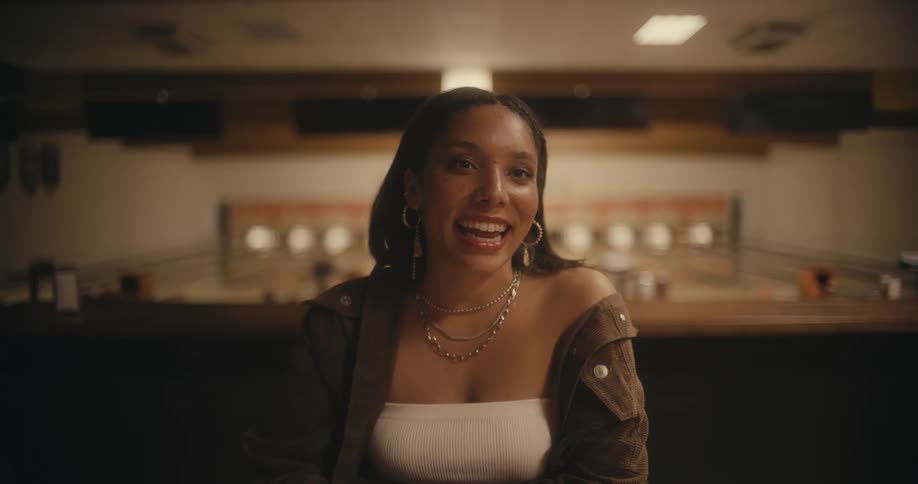 A young woman at a bowling stands at a counter and talks and reaches for her purse