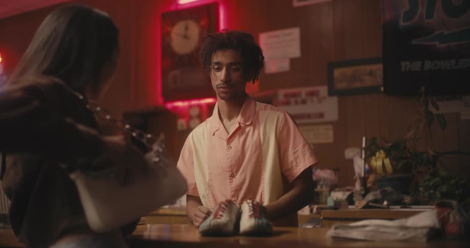 A woman tries to pay for bowling shoes but the man gives them to her for free
