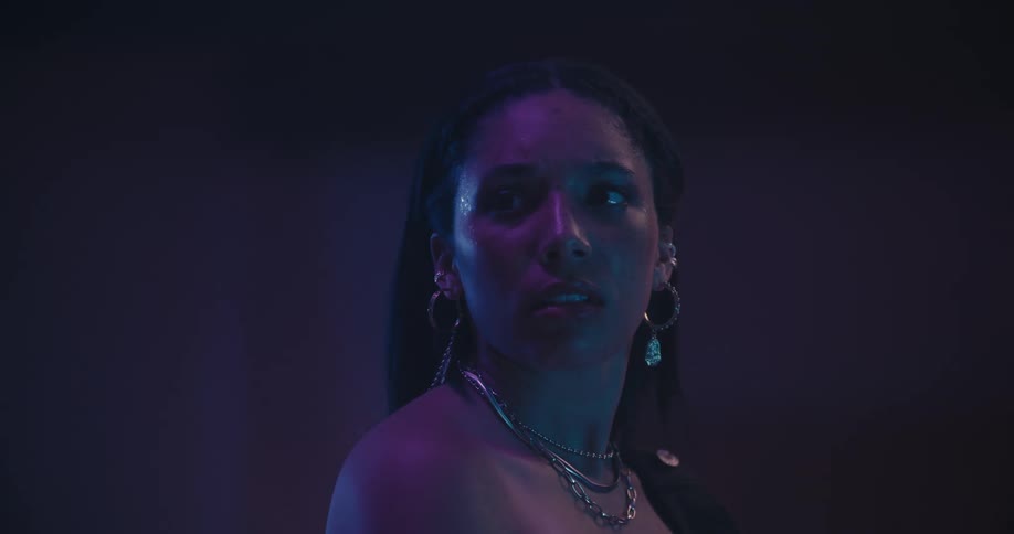 Woman standing under purple lighting turns startled and looks around