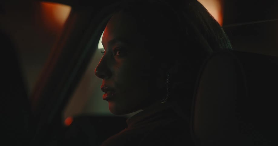 Young woman sitting in the passenger seat of a car approaching someone at the drivers seat to kiss at night