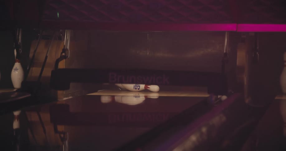 A ball rolls down a bowling alley and knocks down all the pins