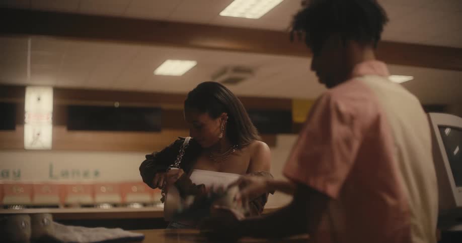 A clerk at a bowling alley gives a woman a pair of shoes and when she goes to get money out of her purse he declines it