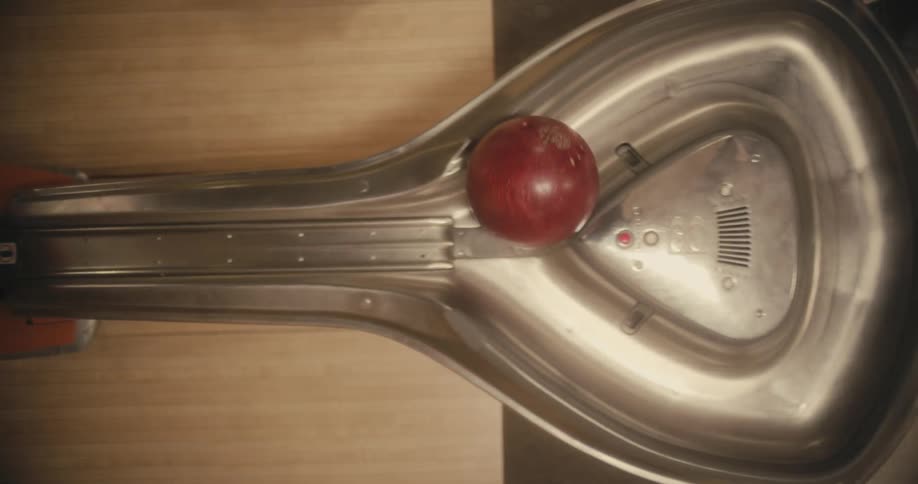 Someone picks up a bowling ball as it rolls out of a machine in a bowling alley