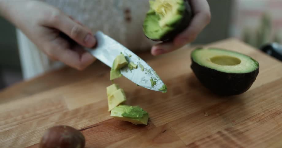 A woman uses a knife to scoop out the diced avocado from its skin