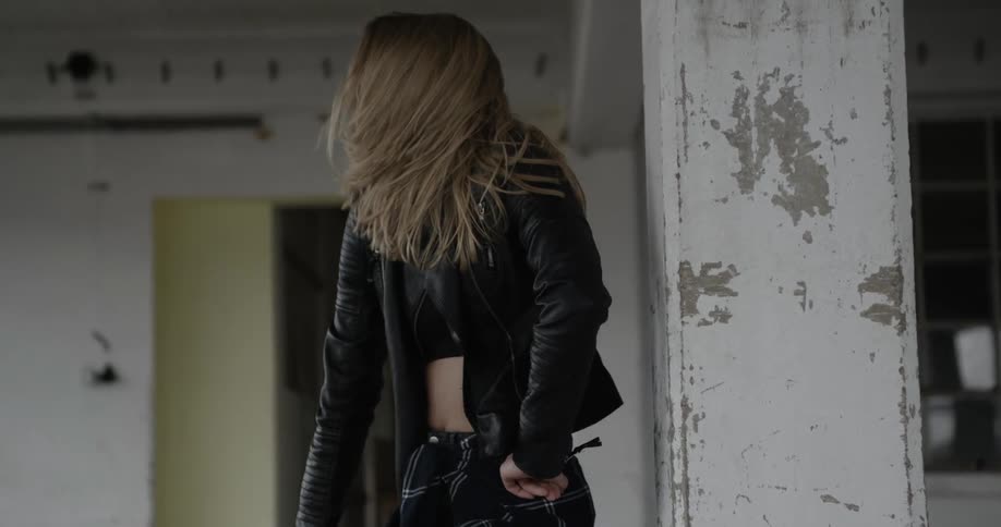 A woman in a jacket dances next to a chipped pillar